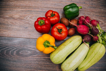 Red tomatoes and colored bell peppers on a dark wooden background. Raw vegetables. Green zucchini with new potatoes and radishes.