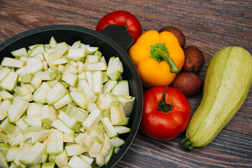 Sliced green zucchini. Red tomatoes and colored bell peppers on a dark wooden background. Raw vegetables. Young potatoes and radishes.