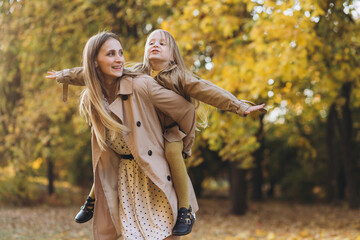 Happy mother and her beautiful daughter have fun and walk in the autumn park.