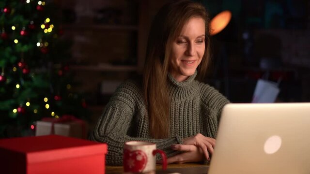 Young woman at home in Christmas time talking on video chat online on laptop computer. Happy and smiling, christmas tree in background.