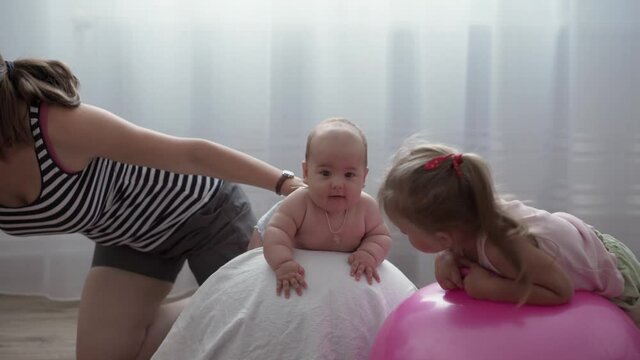 Childhood, Motherhood, games, upbringing, development concept - young mom do exercise, masah with newborn baby on fitball. little daughter girl and boy son play, smile in kid playroom. kids in nursery