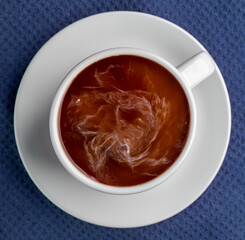 Coffee steaming in a cup with saucer isolated on a blue background looking straight down flat lay