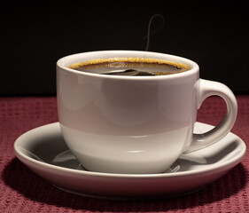 Coffee steaming in a cup with saucer isolated on a black background on a red surface 