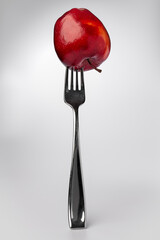 A red apple with a fork stuck in it isolated against a white background