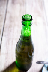 Full green blond beer bottle opened on a wooden surface