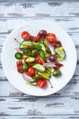 Simple Salad with Green and Kalamata Olives, Cucumber, Cherry and marinated Tomatoes, Capers and Jalapeno Pepper. Bright wooden background.  Top view.  