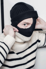 A striped man with a covered head and a hole in his balaclava where his eye can be seen staring at...