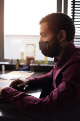 African businessman or developer wearing surgical face mask in the restaurant and typing on laptop - concept on new normal everyday lifestyle and people at work in covid-19 pandemic season.