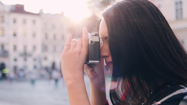 Close up portrait of young woman taking pictures on old camera on city center. Female photographer points the lens and takes picture.Side view