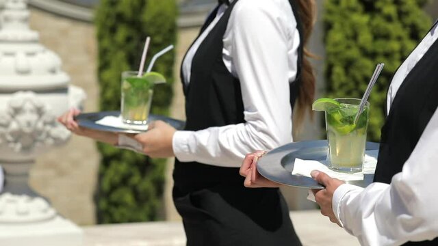 The waiters hold glasses of fresh lemonade and lime wedges on a tray outside on the street. A refreshing drink on a hot summer day.