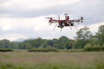 Fototapeta na wymiar Hex copter camera drone hovers in front of a rural background.