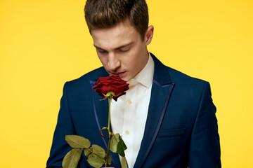 Young man in a classic suit with a red rose in his hand on a yellow background emotions cropped view model