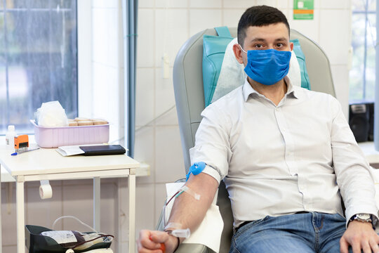 Portrait Of Young Man Donor In Medical Mask From Coronavirus Donation Blood In Laboratory. Prevention Of Covid-19 In Hemodialysis Transfusion Unit In Hospital.