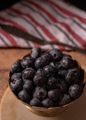 Blueberries in vintage metal bowl on rustic wooden background. Dark mood photo. Selective focus, copy space