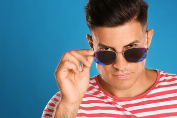 Handsome man wearing sunglasses on blue background, closeup