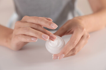 Young woman holding jar of cream at table, closeup