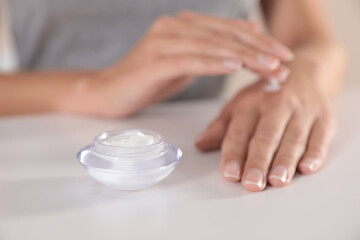 Obraz na płótnie Canvas Young woman applying hand cream at table, closeup