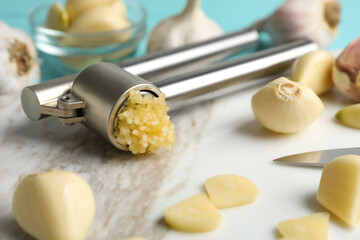 Garlic press and fresh cloves on marble board, closeup. Organic product