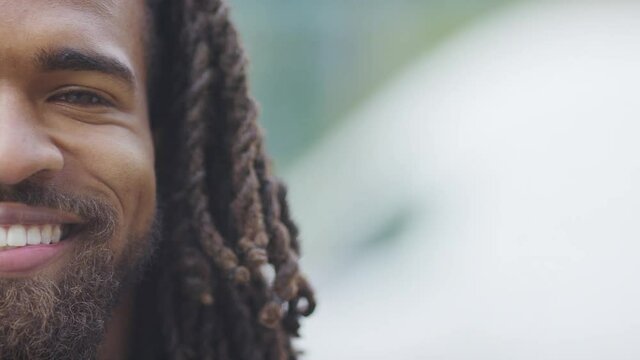 Half face portrait of handsome black male with dreadlocks looking to camera and smiling, in slow motion