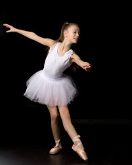Naklejka premium Cute little girl in a tutu and pointe shoes is dancing in the studio on a black background.