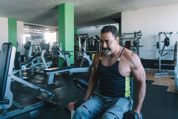 Naklejka premium mature man does shoulder exercises in gym, muscular man