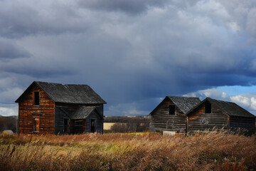 Fototapeta na wymiar An image of an old abandoned homestead and two wooden granaries under dark stormy skies. 