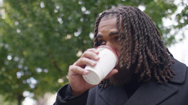 Attractive black male waiting in the city and sipping from a coffee cup, in slow motion