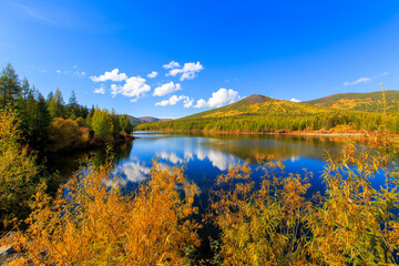 Fototapeta na wymiar The nature of the Magadan region. A beautiful flat surface of the lake against the background of colored hills and the blue sky. Fascinating view of the forest lake