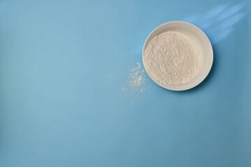 Wheat flour in a white deep plate, a little awake on a blue background.