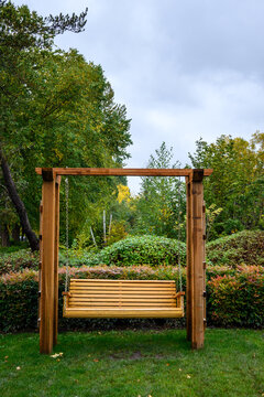 Wooden Bench Swing Hung From A Wood Trellis Outside On A Wet Fall Day
