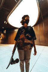 Chica joven urbana con mascarilla coronavirus pandemiua covid-19 en skatepark con patin skate...