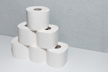 Close-up of toilet paper rolls on white table with background of textured grey wall.