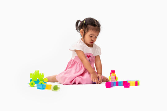 Asian child girl in pink dress siting and play colorful plastic blocks or toy happily isolated on white background