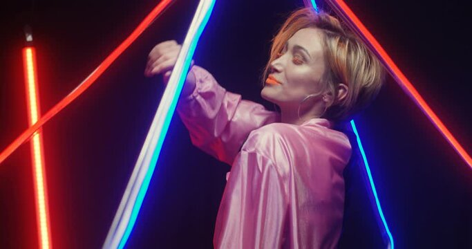 Close up of Caucasian young beautiful woman in extraordinary look with orange lips dancing in astera lamps light. Female pretty dancer in glowing light moving in fast rhythm. Happy cool girl having