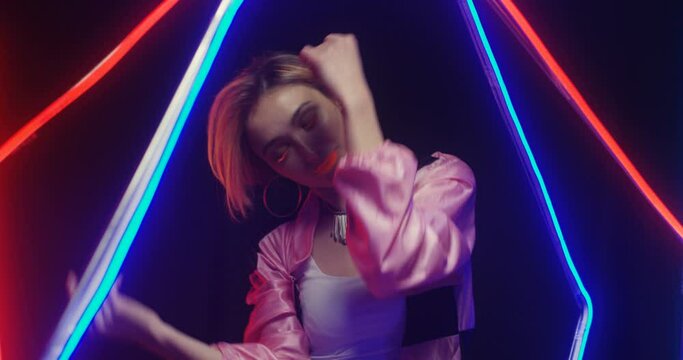 Close up of Caucasian sexy young attractive woman in extraordinary style with orange lips and short fair hair dancing seductively in astera lamps light. Female dancer in glowing light moving with