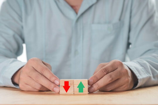 Business increasing or decreasing , Businessman holding green up arrow or red down arrow which print screen on wooden cube block.