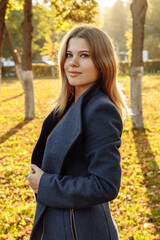 Photo of a blonde in a vertical format. A young woman in a blue coat is lit by the warm autumn sun....
