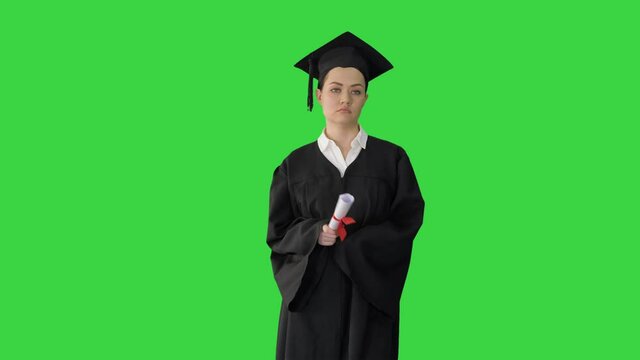 Female Student In Graduation Robe Holding Diploma And Waiving It Around On A Green Screen, Chroma Key.