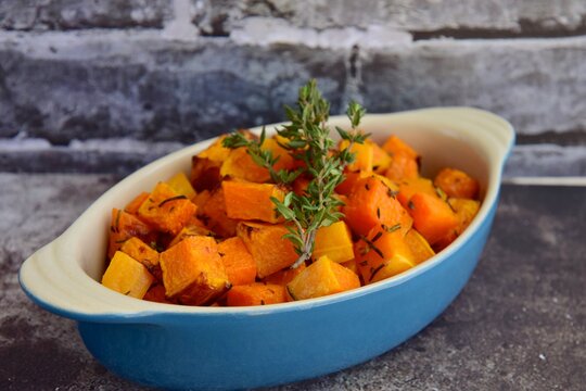 Baked pumpkin cubes with thyme on grey background
