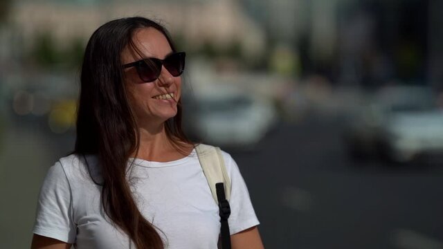 Portrait of a beautiful, dark-haired, smiling, middle-aged woman with dark glasses. It is located on the background of a highway, cars pass by it.