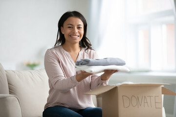 Portrait of smiling African American young woman gather clothes in donation box for those in need. Caring biracial female volunteer put apparel in package for needy people. Reuse, recycle concept. - Powered by Adobe
