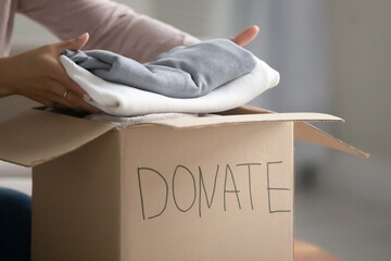 Crop close up of caring female volunteer put gather clothes in box make donation to needy people....
