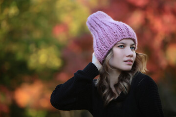 Girl in a pink knitted hat against the background of the autumn forest. Warm woolen headdress bokeh in the background.