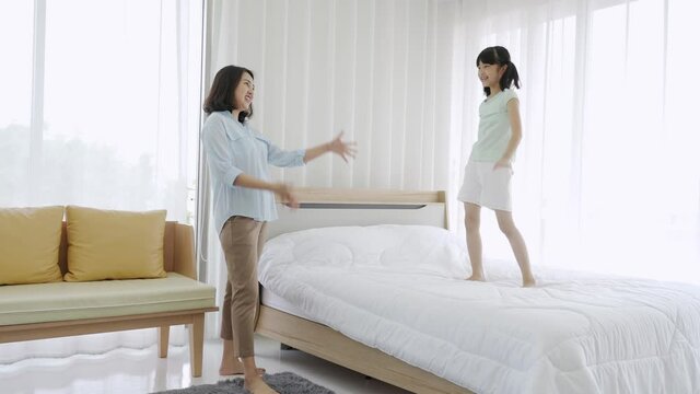 Asian mom and daughter having fun playing dancing in bed room