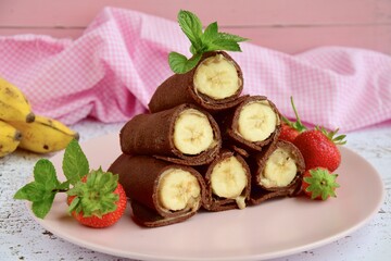 Delicious chocolate crepe rolls with banana and almond butter. Garnish with strawberries and mint leaves