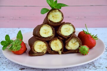 Delicious chocolate crepe rolls with banana and almond butter. Garnish with strawberries and mint leaves