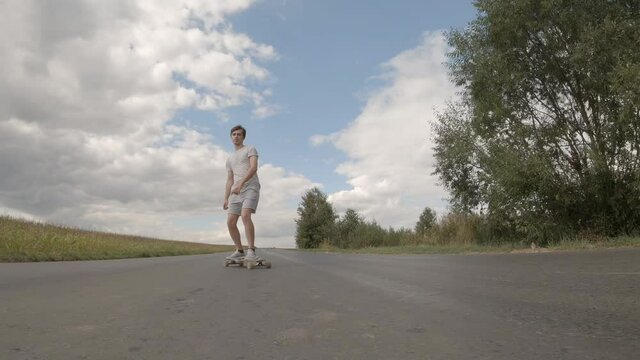 Handsome guy longboarding riding skateboard cruising downhill on countryside road on summer sunny day.