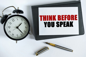 On the table there is a clock, a pen, a notebook and a card on which the text is written - THINK BEFORE YOU SPEAK