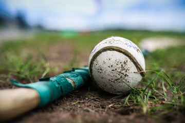 A hurley and a sliothar lie in the grass with a out of focus background - obrazy, fototapety, plakaty