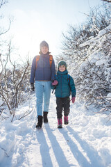 A child with a backpack walks with mother in a snowy forest